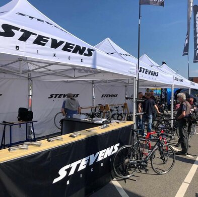 White 3x3m event gazebo customised with Stevens bikes logo at bicycle sporting event with black half-height side walls with counter