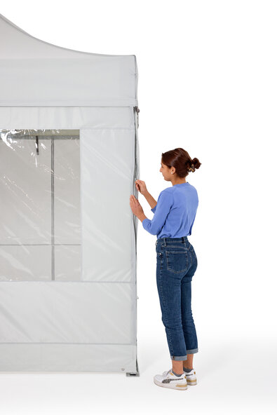 The woman is attaching the side walls to the folding gazebo. She closes them with a zip for complete all-round protection.